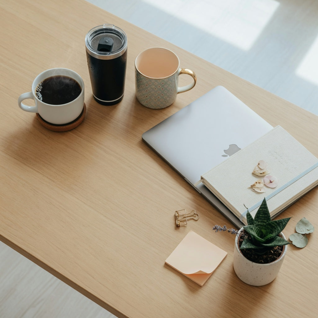 Three of the best coffee mugs for coworkers on an office desk: a round desk mug, an insulated commuter tumbler, and a patterned gift mug beside a laptop.