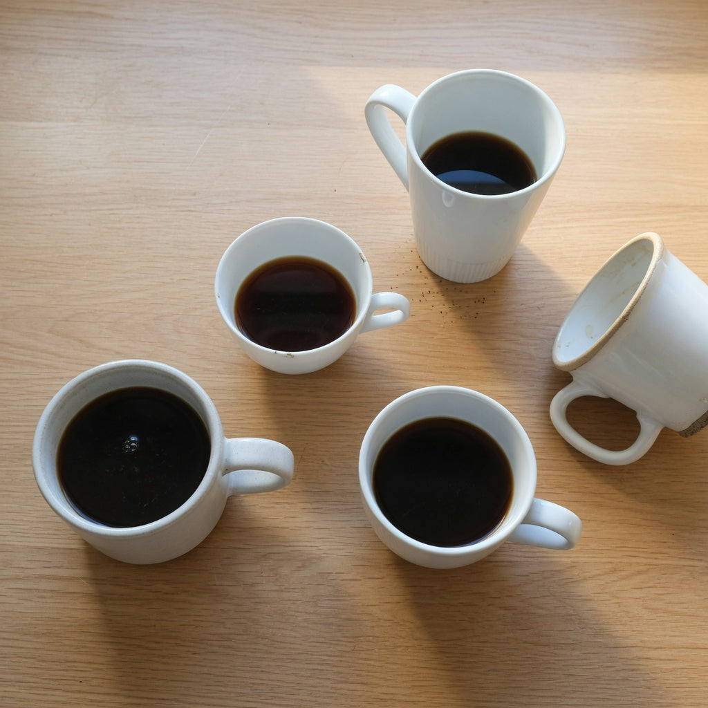 Plain white coffee mugs of different heights and materials lined up on a kitchen counter, illustrating the size and material comparisons in our guide to the best plain white mugs for everyday coffee