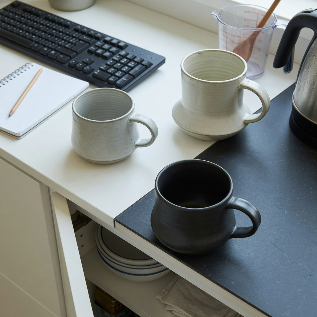 Comparison of ceramic wide bottom coffee mugs buying priorities using three mug shapes beside a measuring cup, keyboard, and cabinet shelf