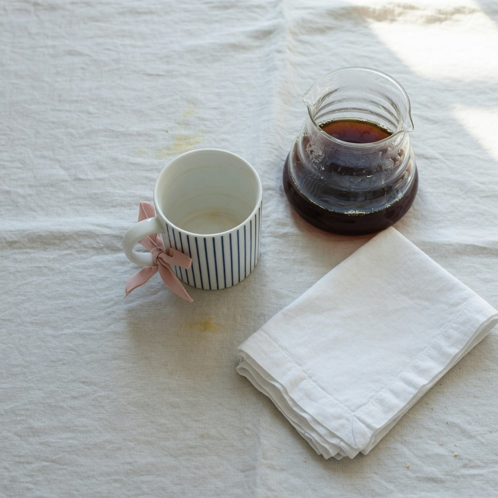 A preppy ceramic coffee mug with navy stripes and a blush bow on a linen brunch table
