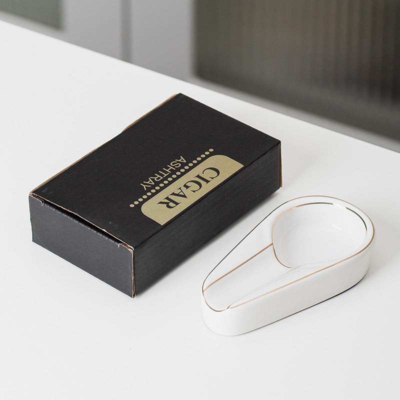 White ceramic cigar ashtray with a gold-colored rim beside its actual English carton