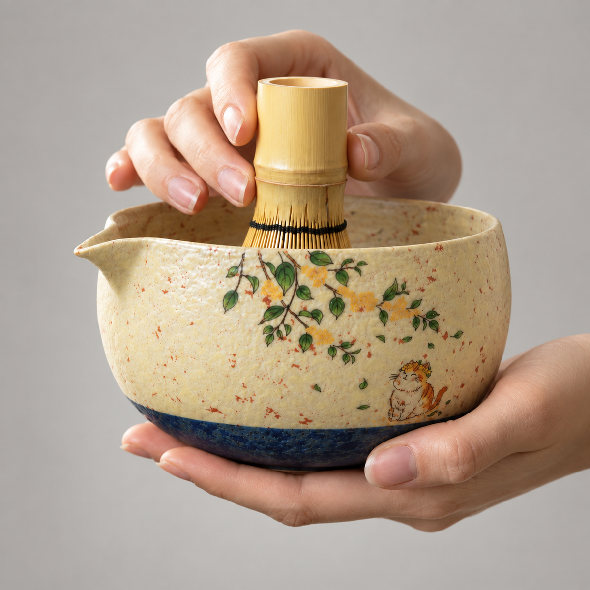Hands demonstrating the cat and blossom matcha bowl; bamboo whisk is a demonstration prop and is not included