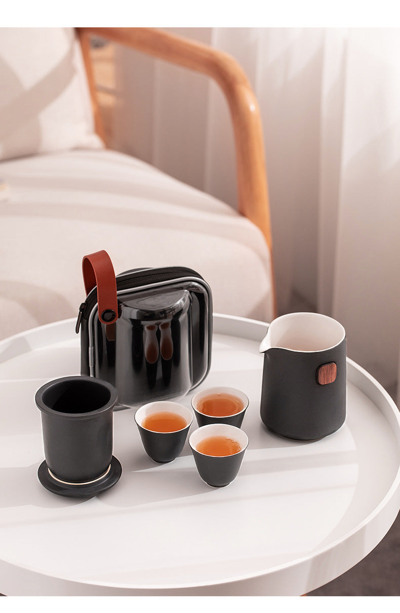 Black ceramic server and three cups of tea beside the removable infuser resting on the reversed lid, with carrying case