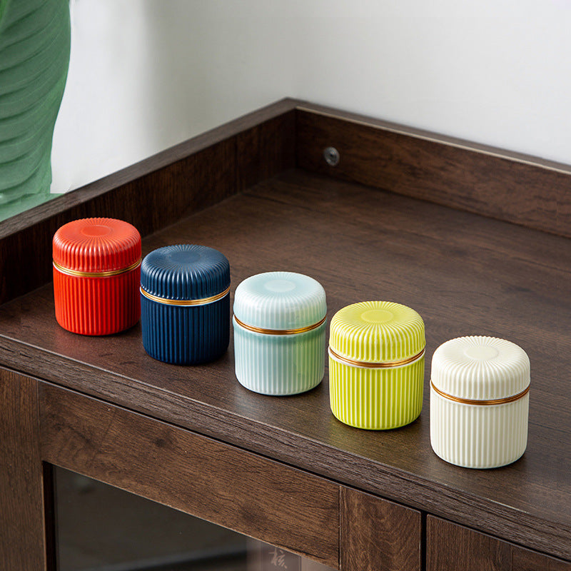 Five ribbed ceramic tea jars in orange-red, navy, pale blue, yellow-green and ivory