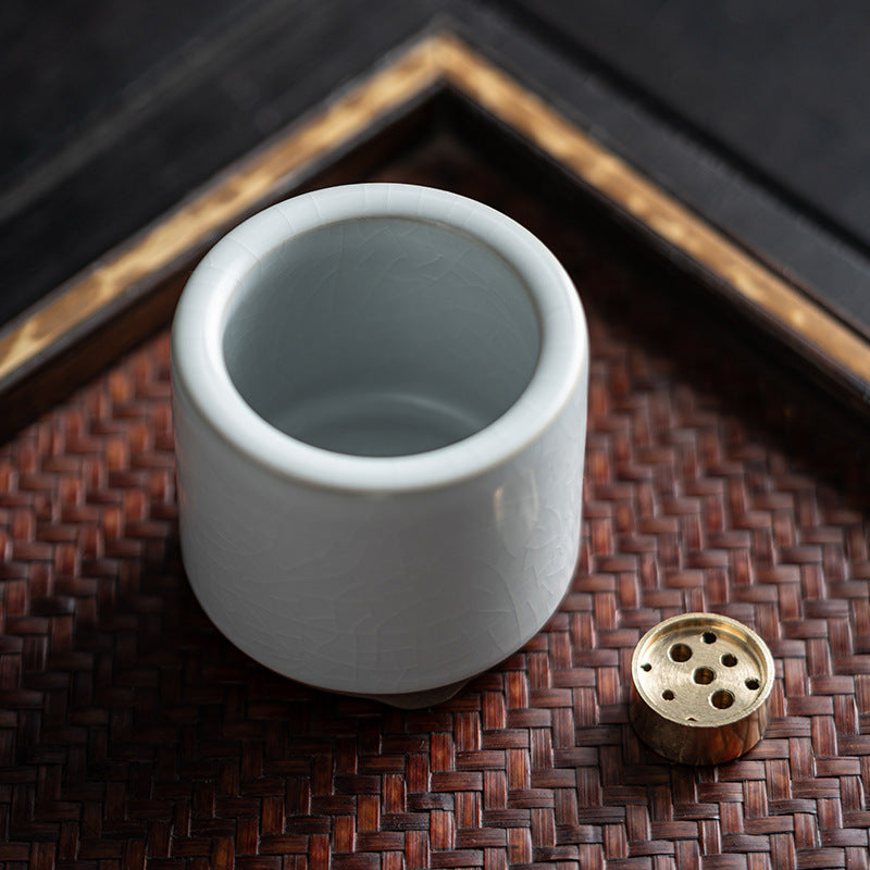 Open ceramic incense holder beside a metal incense support