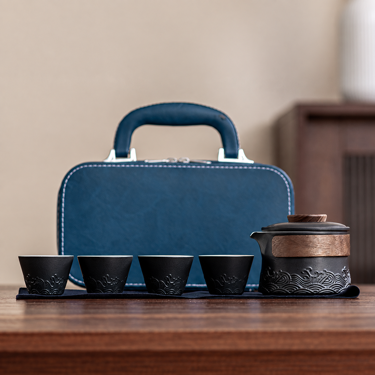 Black wave-relief ceramic brewer with four cups and blue carrying case