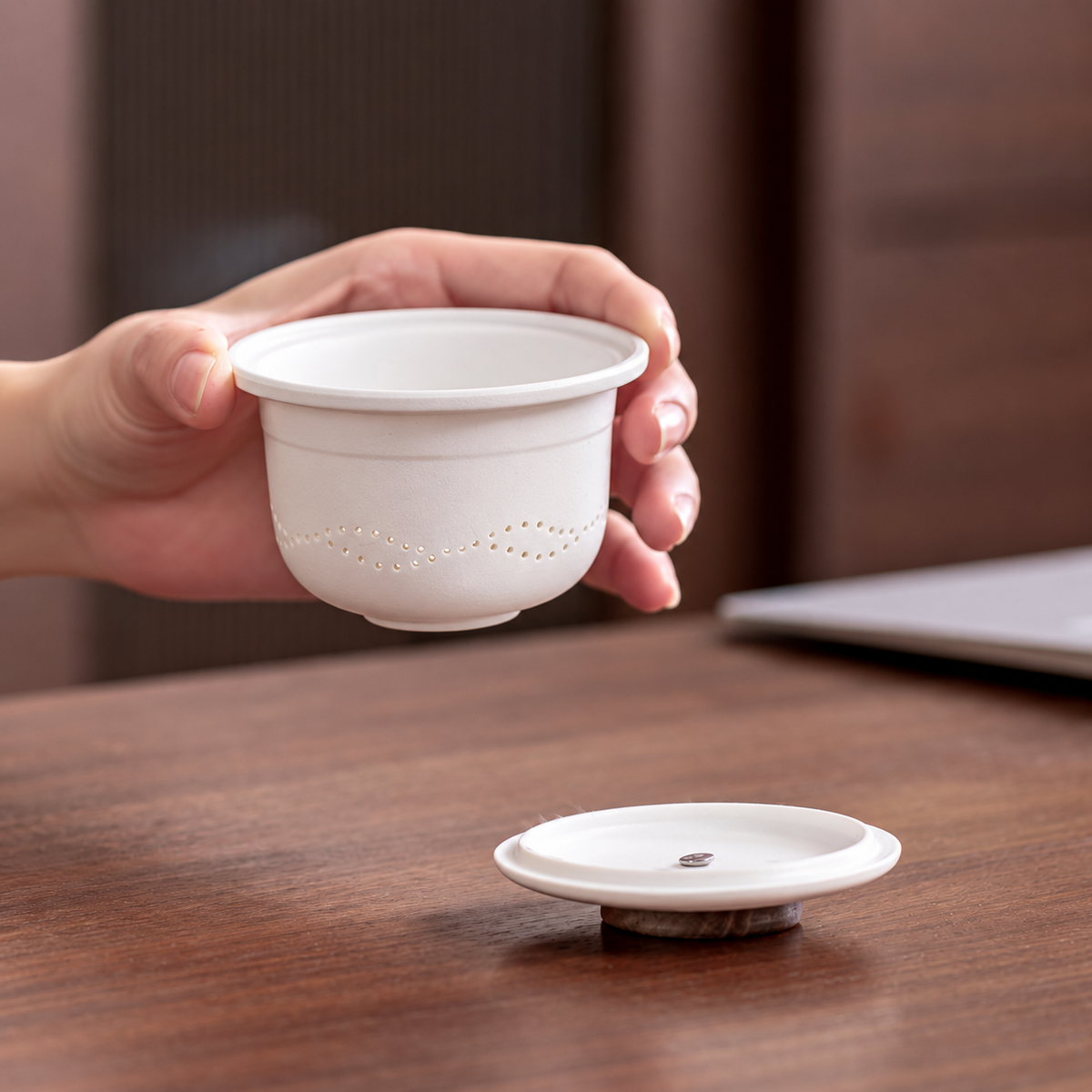 A hand lifting the white ceramic infuser, showing the wavy rows of strainer holes