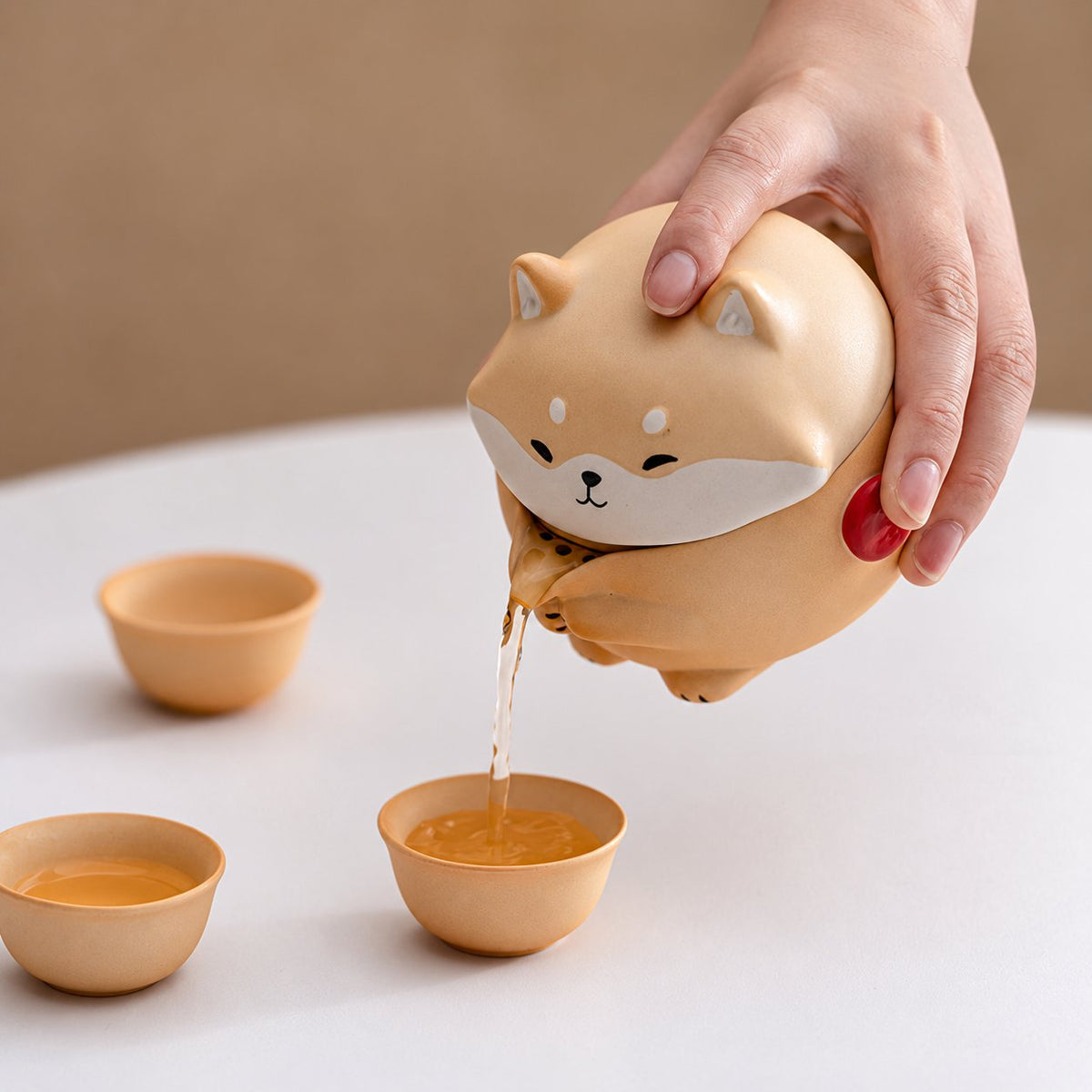 A hand pours tea from the Shiba dog teapot into a matching cup