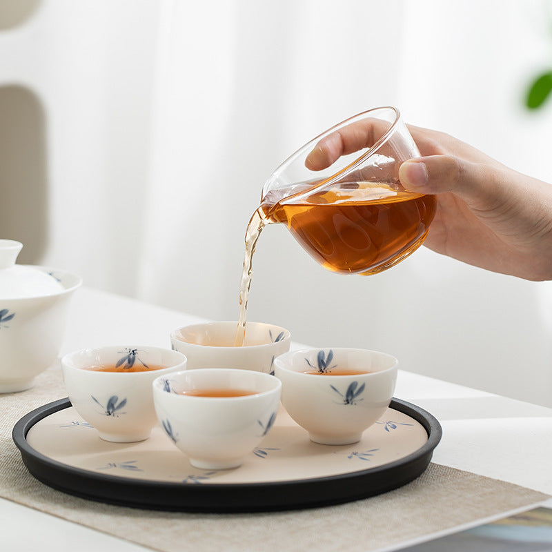 Hand pouring tea from the glass pitcher into four blue butterfly cups on the matching tray