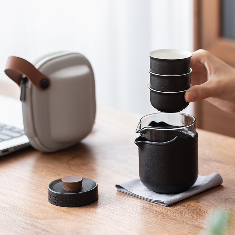 Hand lifting three stacked black cups from the nested glass and ceramic travel brewer