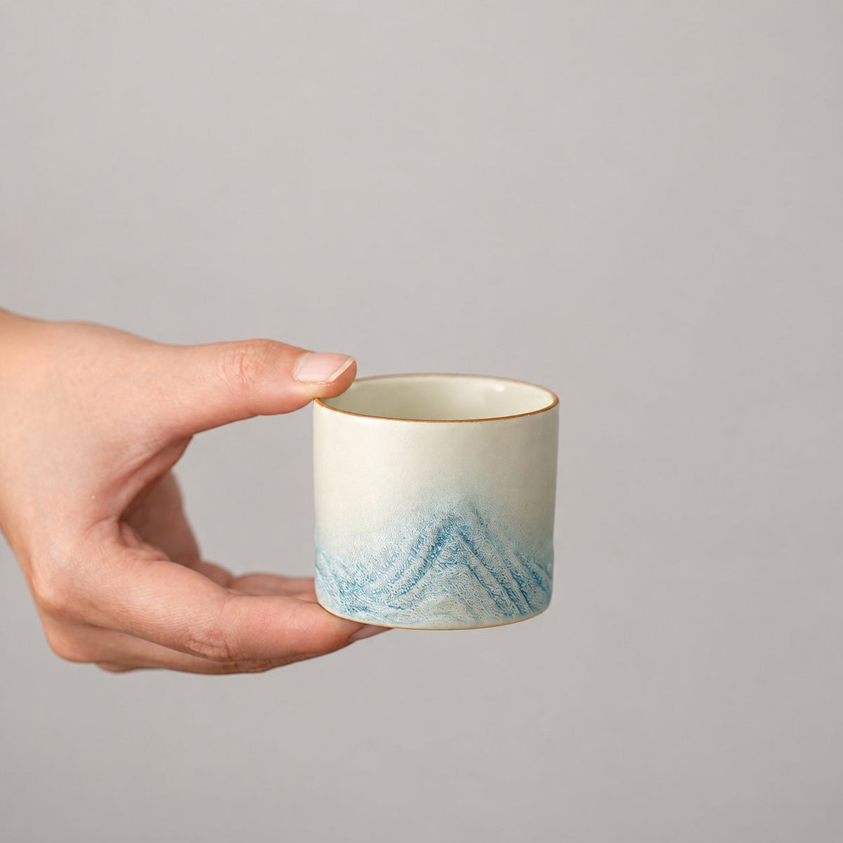 Small ivory ceramic tea cup with pale blue mountain relief
