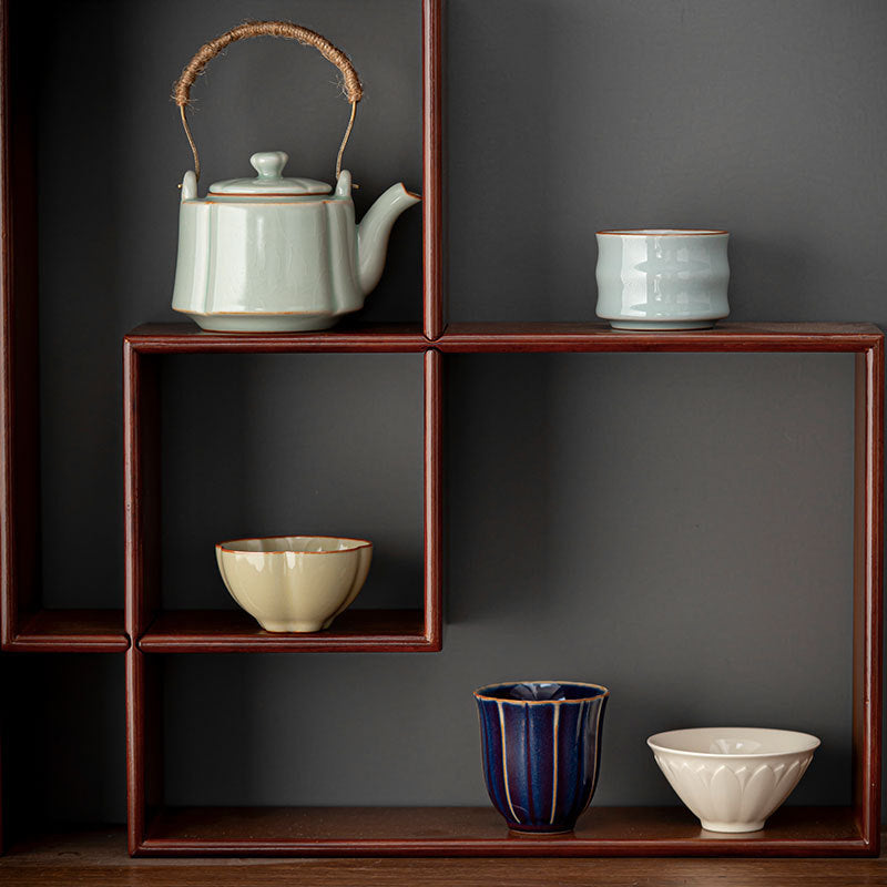Top handle celadon teapot and four contrasting tea cups displayed on a wooden shelf