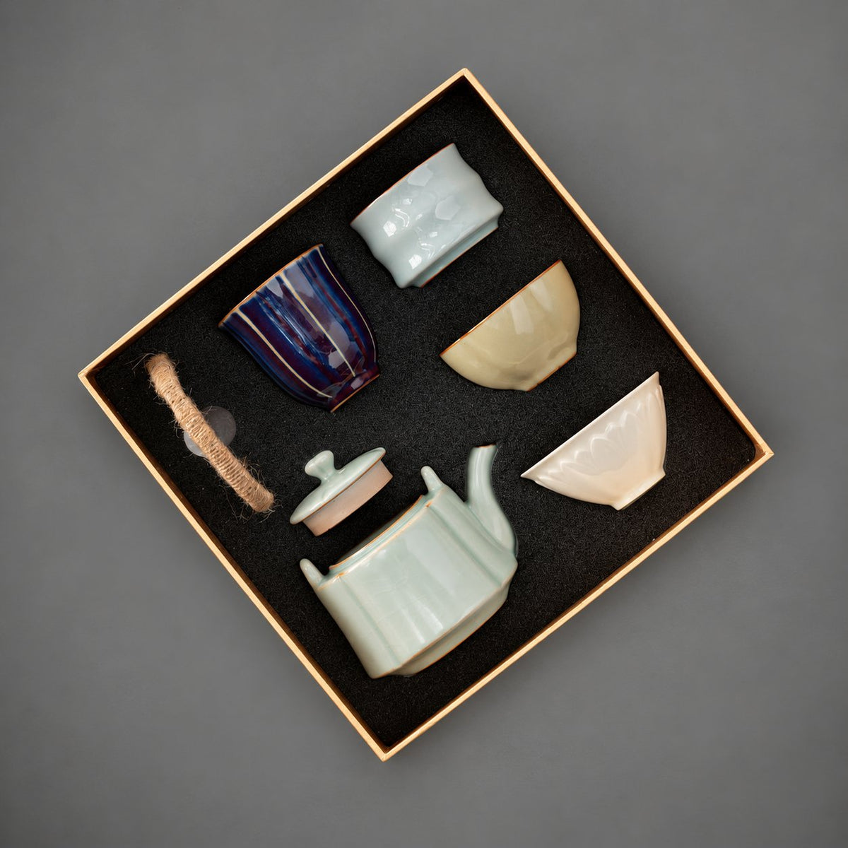 Open gift tray with a celadon top-handle teapot and four distinct glazed tea cups