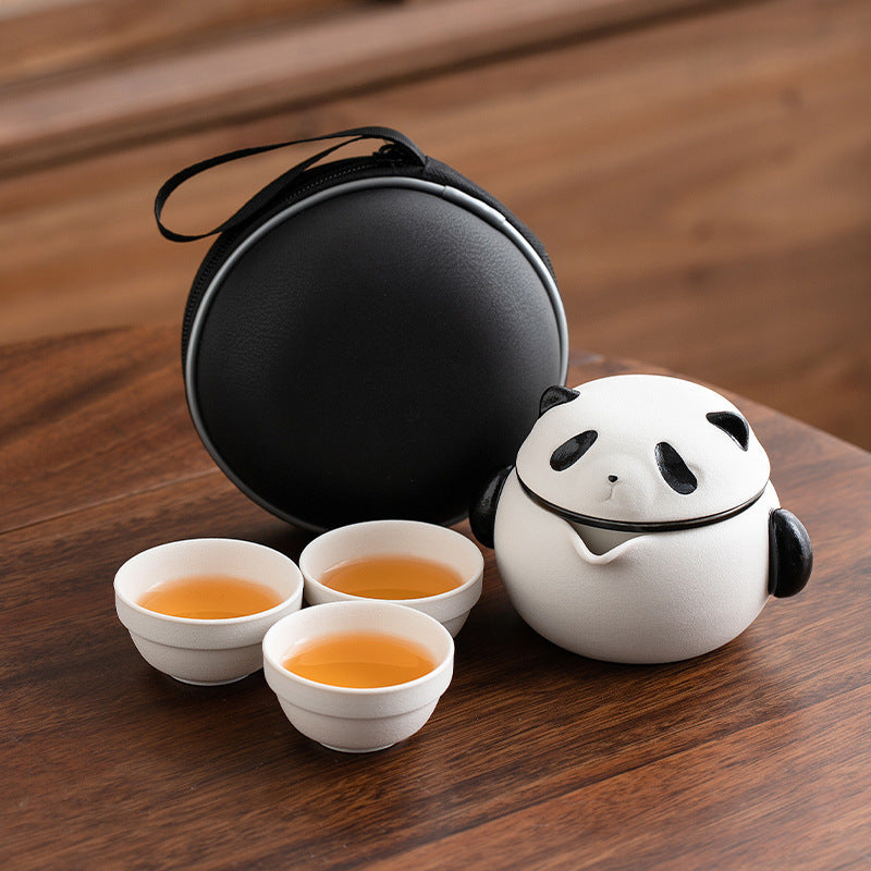 Panda ceramic tea brewer and three cups with a round black carrying case on a wooden table