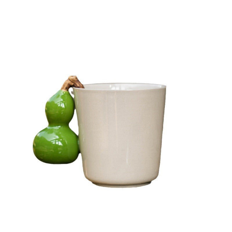 Cream ceramic mug with a glossy green gourd shaped handle on white