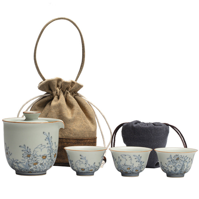 Rabbit-pattern ceramic brewer, three cups and both cloth carrying pouches on a white background