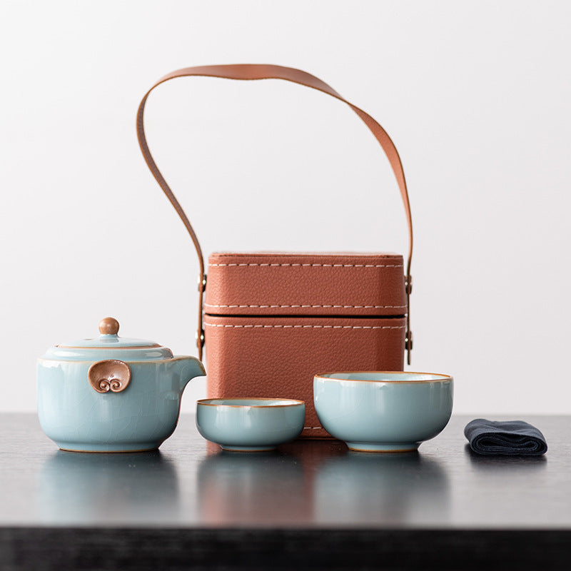 Sky blue ceramic travel teapot with two nesting cups, cloth and brown handled case