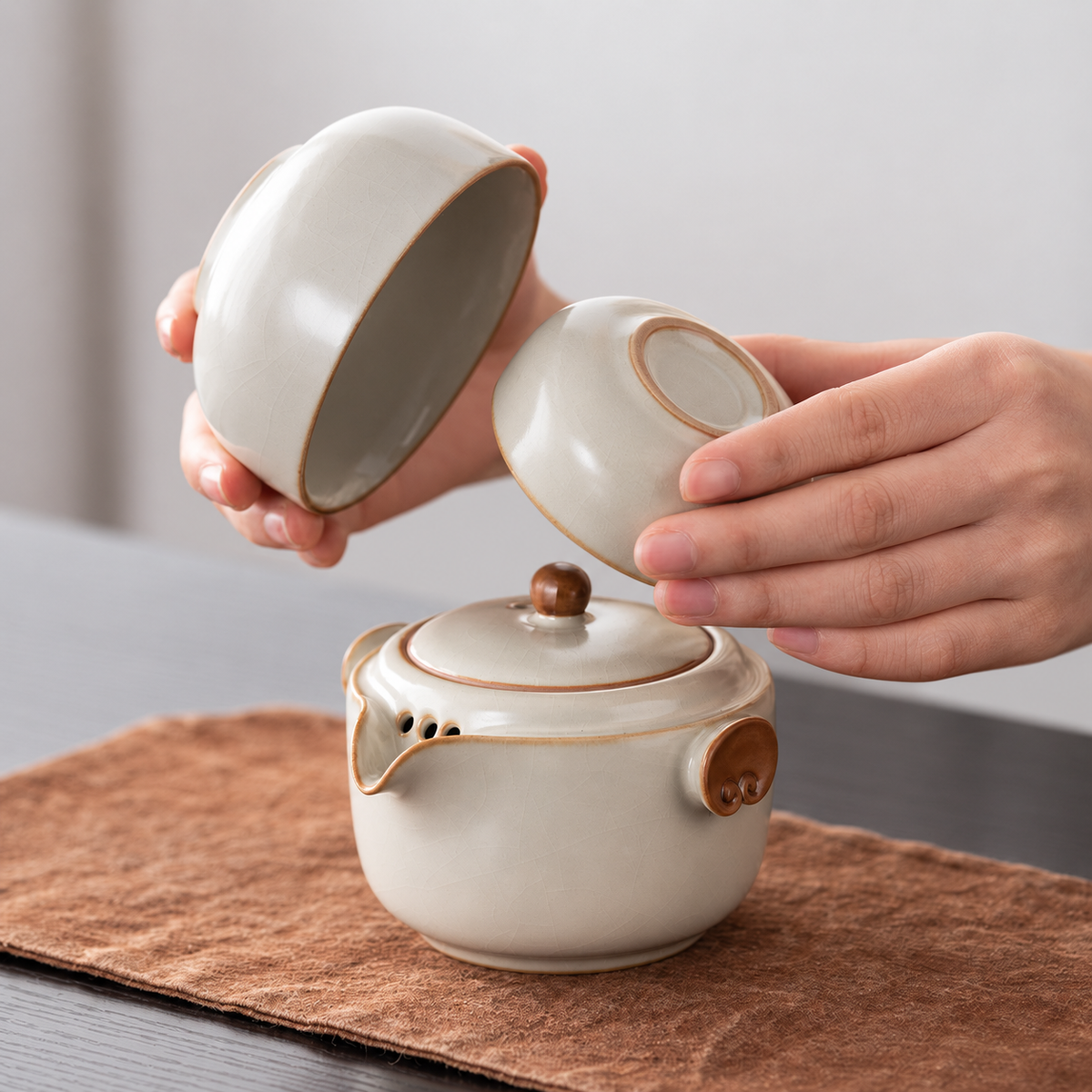 Hands holding the two nesting cups above the matching ceramic travel teapot