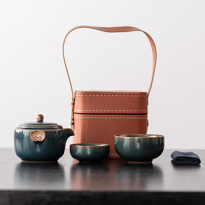 Deep teal ceramic travel teapot with two nesting cups, cloth and brown handled case