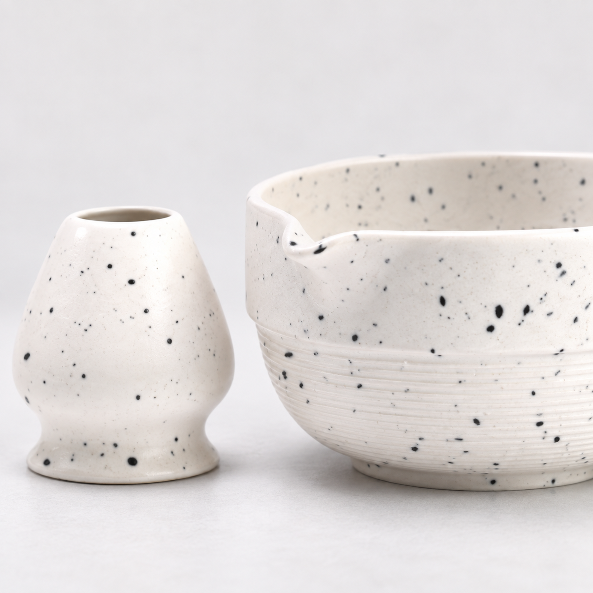 Close view of the speckled white glaze, fine horizontal bowl ridges, pouring spout and matching holder