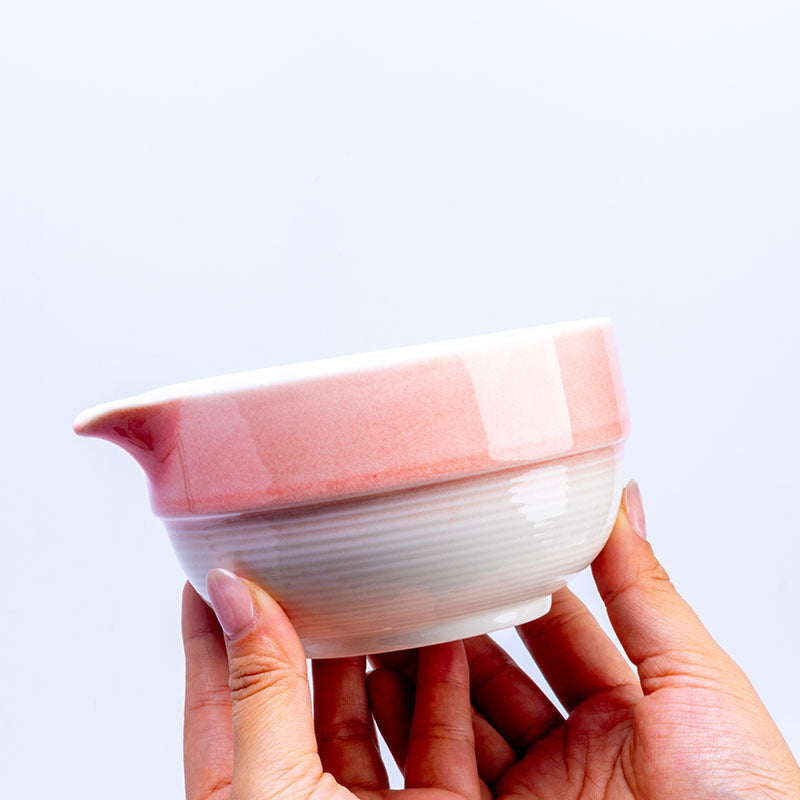 Hands holding the pink and white banded bowl to show its pouring lip and fine lower ridges
