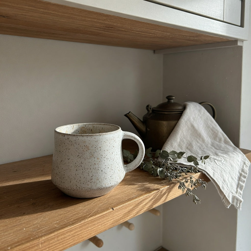 Ceramic tea mug for home decor left on an open kitchen shelf beside a kettle