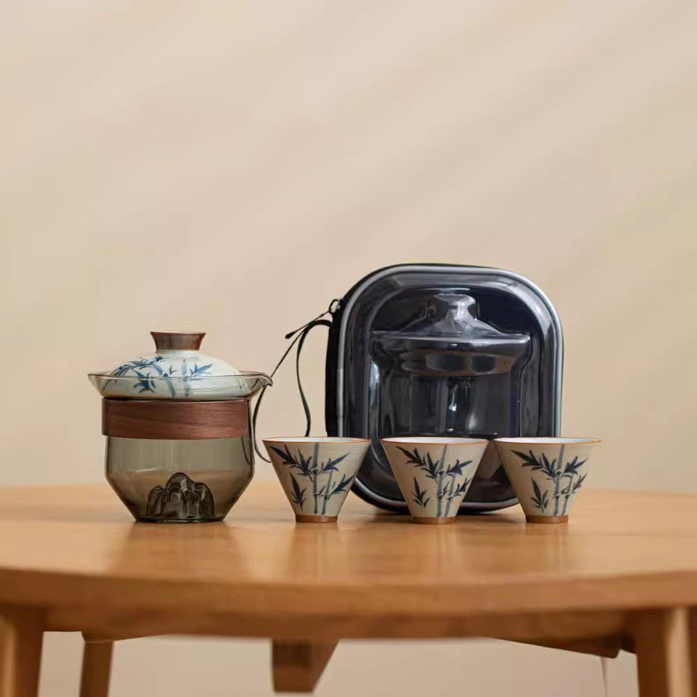 Glass travel tea set with patterned cups: wood-wrapped glass brewer, patterned ceramic lid, three matching patterned cups, and black zippered carrying case with clear front.