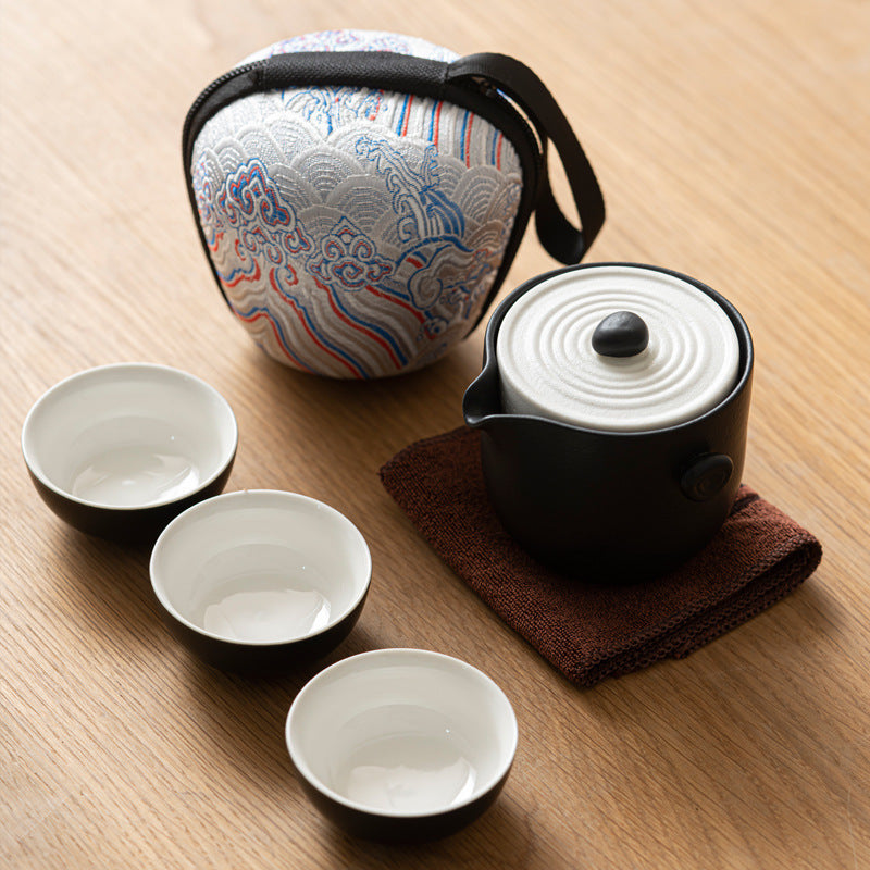 Compact nesting ceramic travel tea set with three cups nested inside a black ceramic brewing vessel next to its patterned zip case.