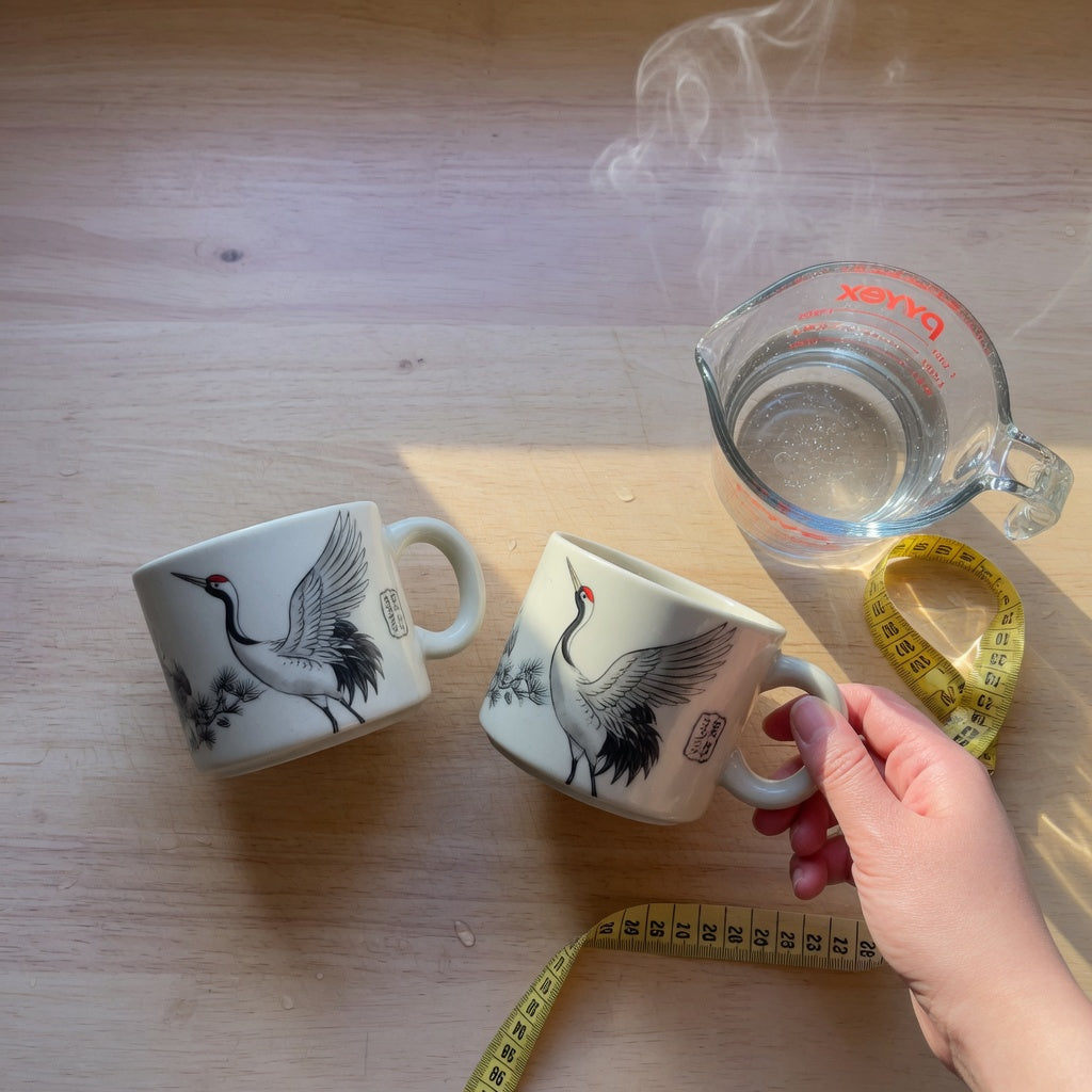 Crane mug comparison: two ceramic mugs with crane bird designs side by side on a wooden kitchen counter