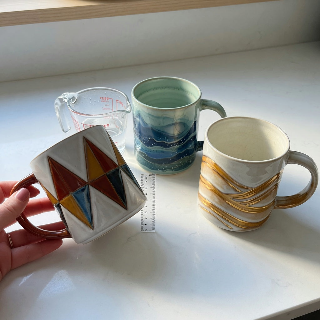 Unique pottery coffee mugs first time buyer practical purchase checklist with three CoffeifyMug designs, a measuring cup, and a ruler on a kitchen counter
