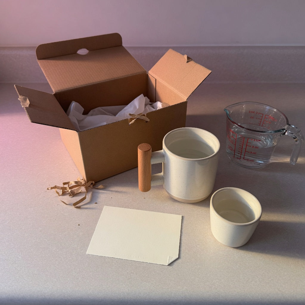 Wooden handle mug gift checklist on a kitchen counter with a wood-grip mug, a smaller cup, a care card, and an open gift box