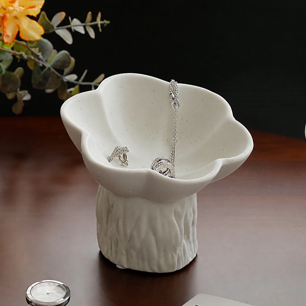 White speckled flower-shaped ceramic jewelry dish on a textured pedestal