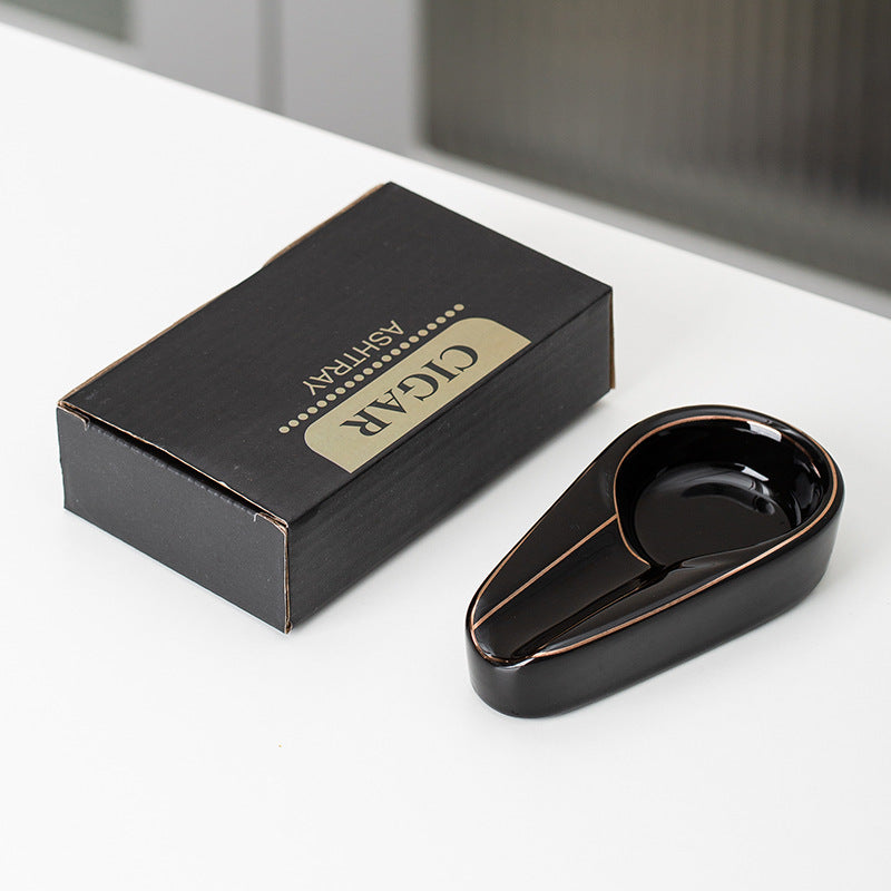 Black ceramic cigar ashtray with a gold-colored rim beside its actual English carton