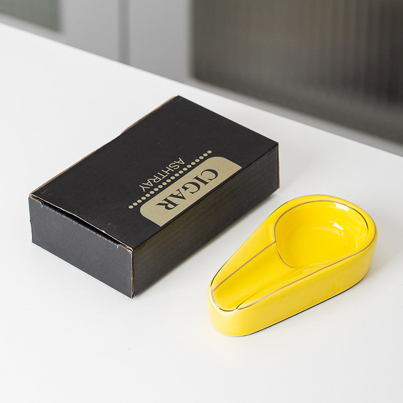 Yellow ceramic cigar ashtray with a gold-colored rim beside its actual English carton