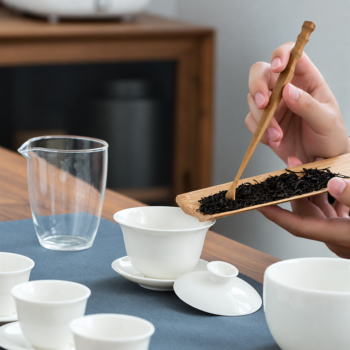 Hands adding loose leaf tea to the white porcelain gaiwan with bamboo tools