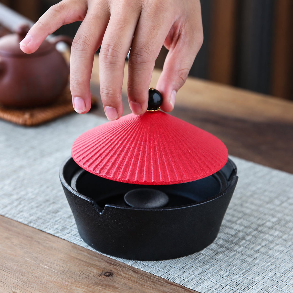 Hand lifting the red lid from a black ceramic ashtray