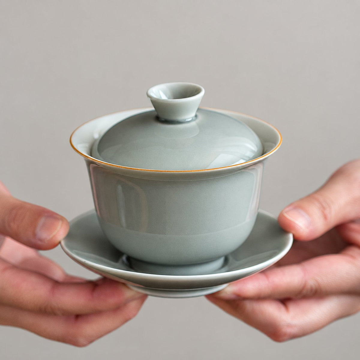 Rounded grey ceramic gaiwan with lid and saucer held in hands