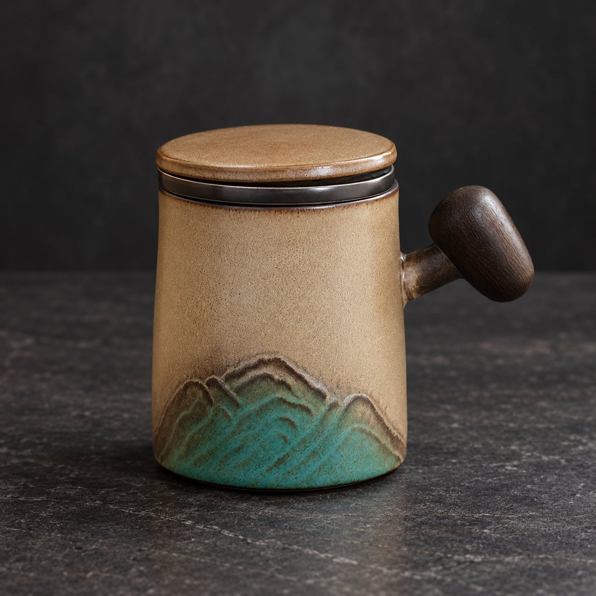 Mountain relief ceramic infuser mug with tan and turquoise glaze on a dark tabletop