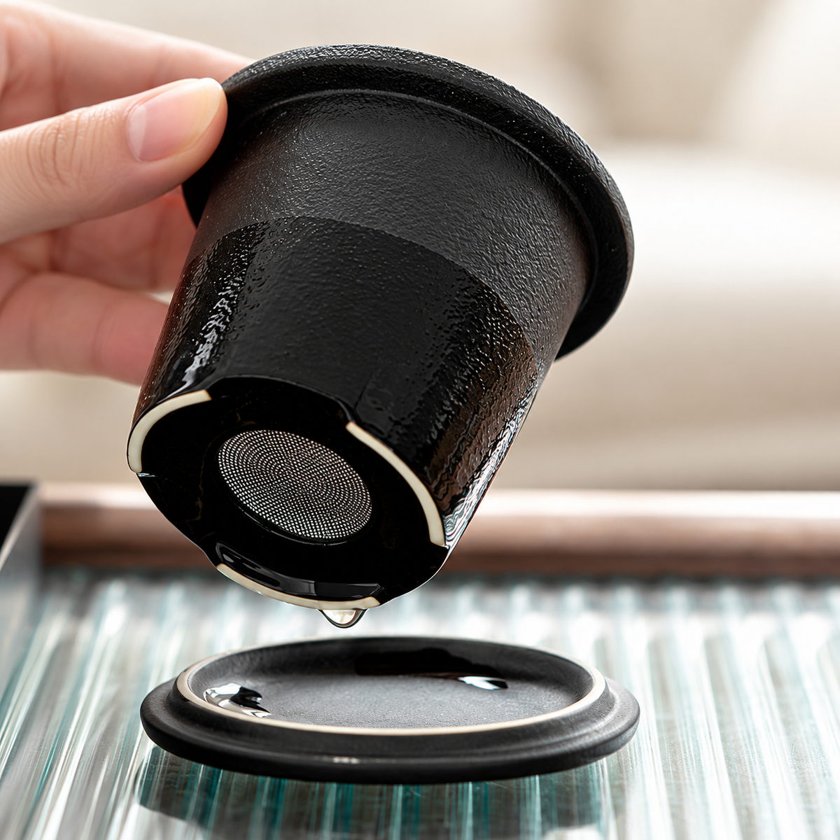 Close view of the removable black ceramic tea infuser with its fine metal mesh base, held above the matching lid.