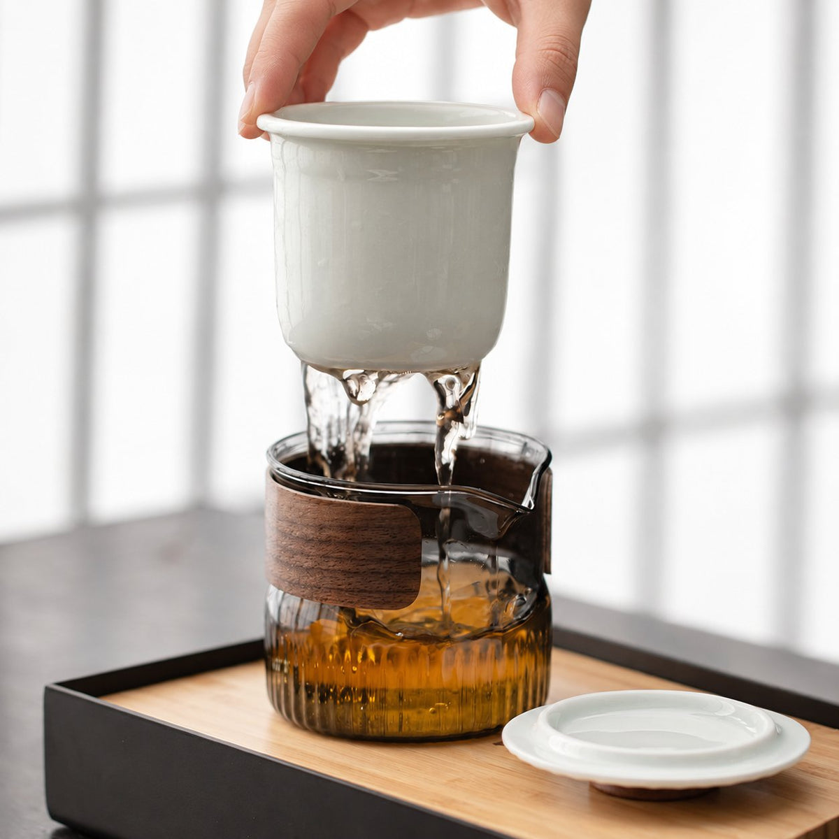 White ceramic infuser draining tea into the ribbed glass pitcher