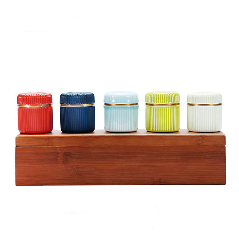 Five small ceramic tea jars arranged on their closed bamboo presentation box