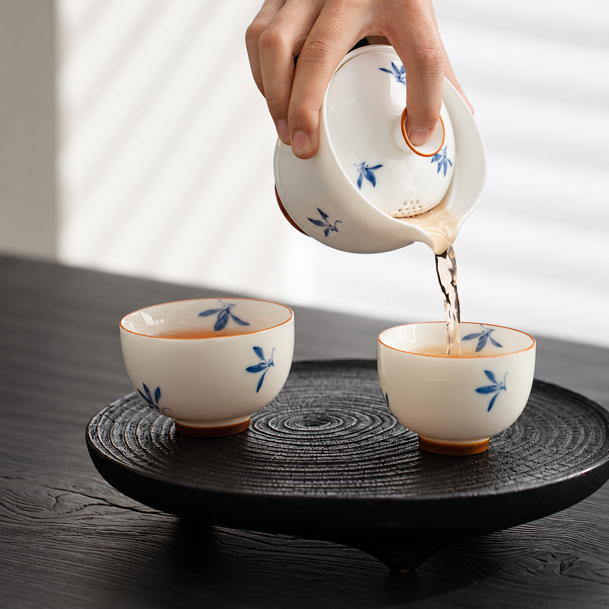 A hand pouring tea from the blue floral brewer into one of the two cups
