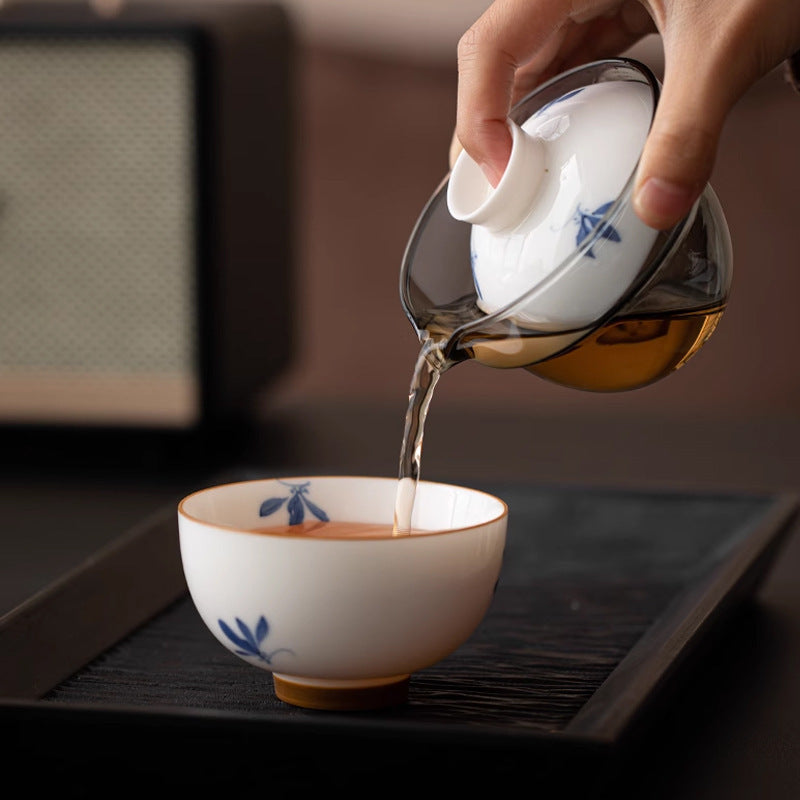 Glass brewing pot pouring tea into a blue orchid ceramic cup