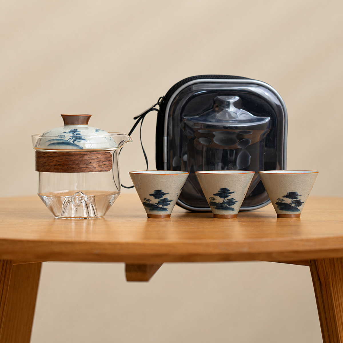 Landscape / Clear glass tea brewer with three patterned ceramic cups and a black travel case