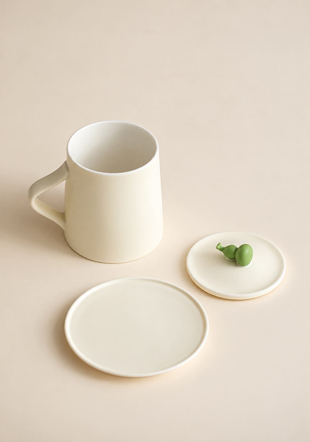 Cream ceramic mug shown empty beside its matching green-gourd lid and saucer; no infuser is included