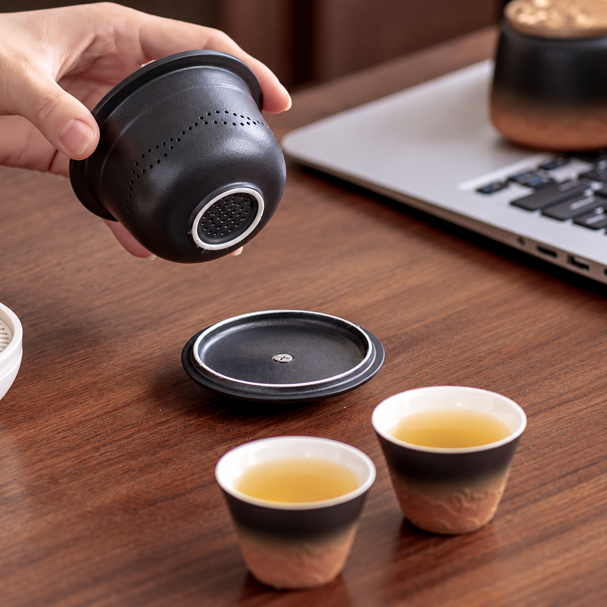 A hand showing the side and base perforations of the black ceramic tea infuser