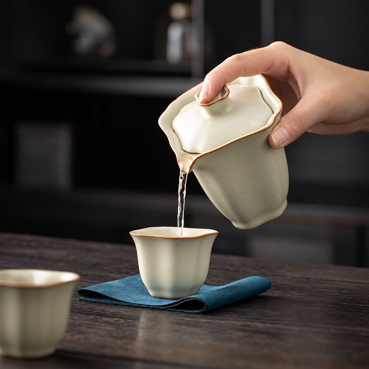 Hand pouring tea from the square crackle-glazed brewer into its matching cup