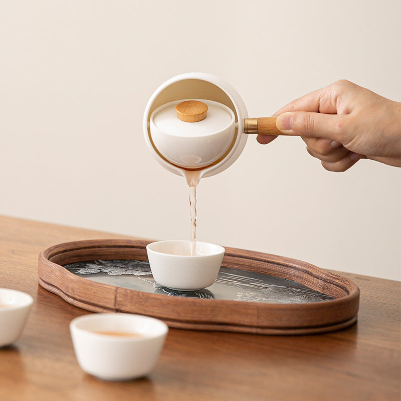 A hand tilting the side-handle tea brewer while its suspended infuser stays upright