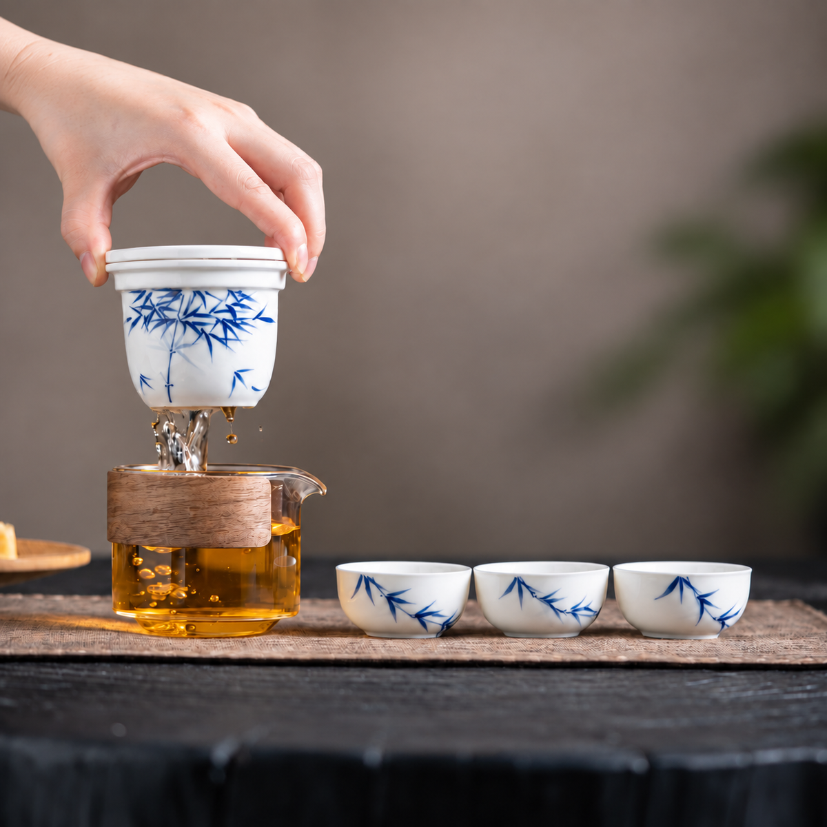 Hand lifting the blue bamboo ceramic infuser above the glass server with three matching cups