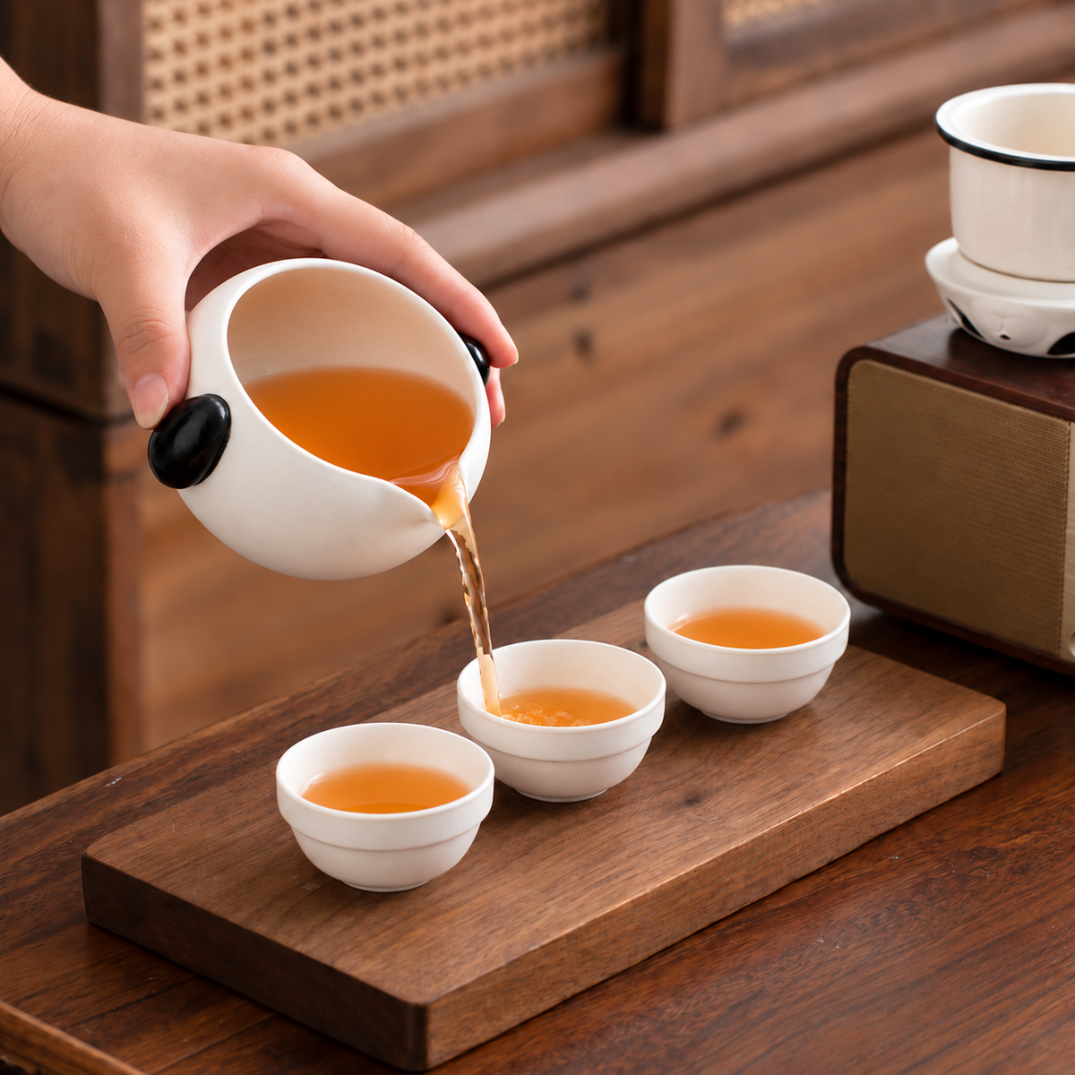 Hand pouring tea from the panda-shaped server into one of three white cups